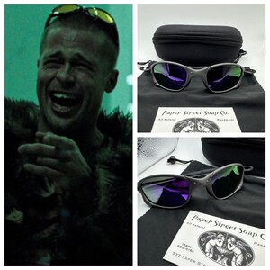 May include: A pair of black sunglasses with purple mirrored lenses. The sunglasses are in a black case with a black drawstring bag. The case has a white label that says "Paper Street Soap Co. All Natural Handmade".