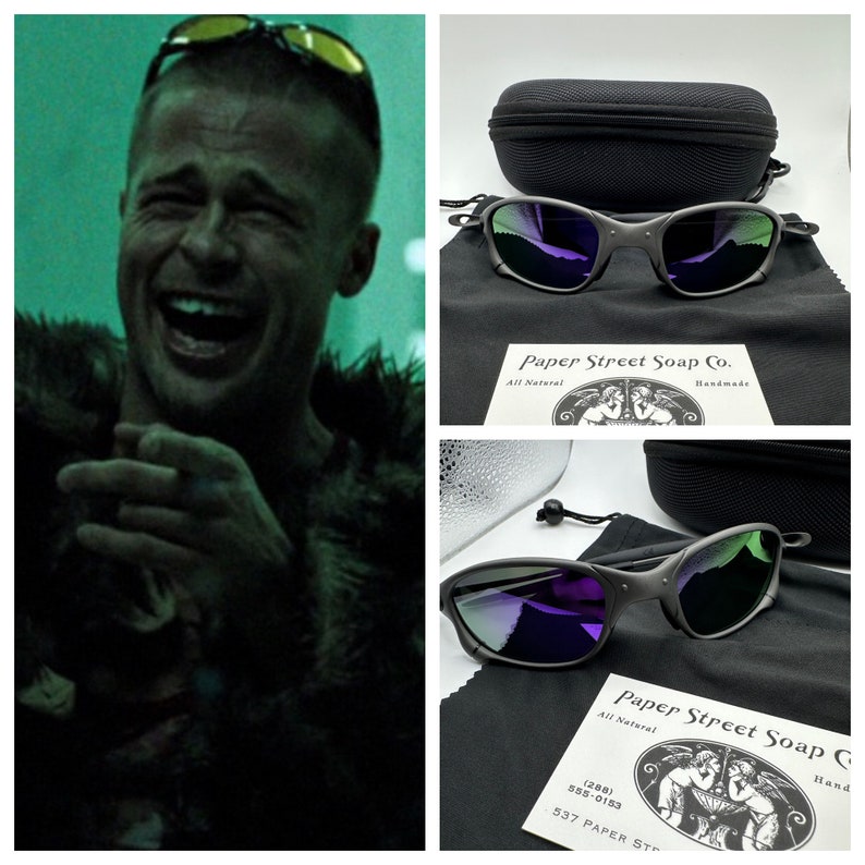 May include: A pair of black sunglasses with purple mirrored lenses. The sunglasses are in a black case with a black drawstring bag. The case has a white label that says "Paper Street Soap Co. All Natural Handmade".