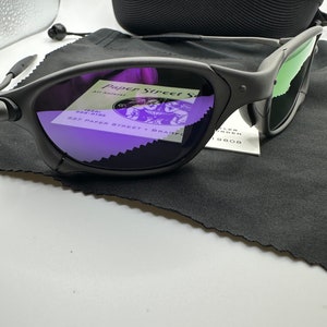 May include: Black sunglasses with green mirrored lenses and a black case. The sunglasses have a purple reflection in the lenses, showing a business card with the text "Paper Street" and "537 Paper Street, Bradford, PA 19808".