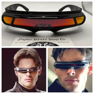 May include: Black visor-style sunglasses featuring a single continuous wrap-around lens with a reflective red-orange tint. The frame is constructed from a solid black material with a thick, structured brow bar and integrated side temples.