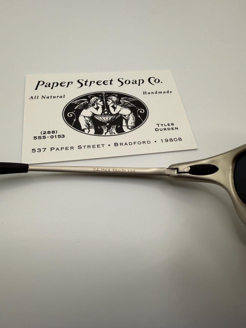 Peut inclure: Lunettes de soleil argent&eacute;es avec des branches et des verres noirs. Une carte de visite de Paper Street Soap Co. est pr&eacute;sente, avec une illustration de ch&eacute;rubins et les mentions "All Natural" et "Handmade".