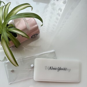 May include: Two clear plastic envelopes, one with a white background and the text "New Years Day" printed in black. The other envelope is empty.