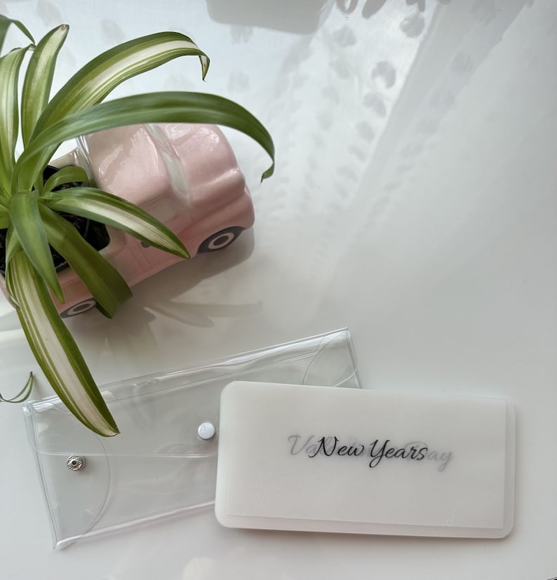 May include: Two clear plastic envelopes, one with a white background and the text "New Years Day" printed in black. The other envelope is empty.
