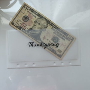 May include: A white envelope with a clear plastic window, containing a $10 bill. The envelope has the word "Thanksgiving" written on it.