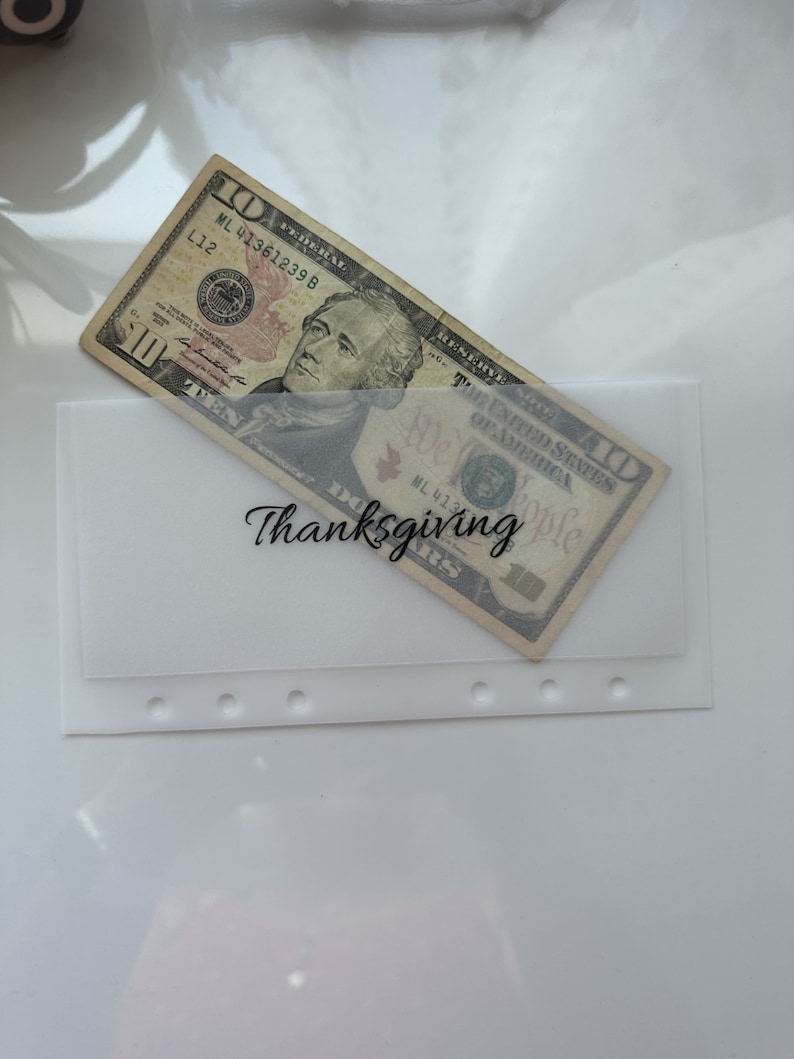 May include: A white envelope with a clear plastic window, containing a $10 bill. The envelope has the word "Thanksgiving" written on it.