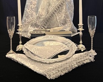 May include: A display of wedding accessories, including a white paisley shawl draped on a mannequin, two champagne flutes, candles, a serving tray, and a matching face mask. The items are arranged on a black surface.