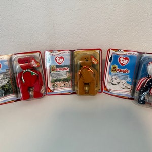 May include: Four Ty Beanie Baby plush toys in their original packaging. The toys are "Osito", "Germania", "Spangle", and "The Bear". Each toy is wearing a different country's flag.