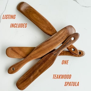 May include: A collection of teakwood spatulas. The spatulas are a warm brown color and have a smooth finish. One spatula has the text "are you bread-y for it" engraved on it. The image also includes the text "ONE TEAKWOOD SPATULA".