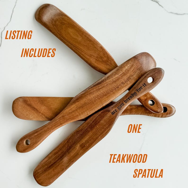 May include: A collection of teakwood spatulas. The spatulas are a warm brown color and have a smooth finish. One spatula has the text "are you bread-y for it" engraved on it. The image also includes the text "ONE TEAKWOOD SPATULA".