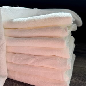 Puede incluir: Una pila de pa&ntilde;os de muselina de algod&oacute;n blanco, doblados cuidadosamente. Los pa&ntilde;os son suaves y absorbentes, perfectos para limpiar y secar.