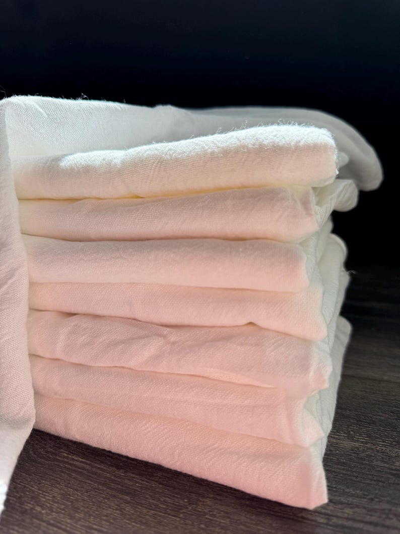 Puede incluir: Una pila de pa&ntilde;os de muselina de algod&oacute;n blanco, doblados cuidadosamente. Los pa&ntilde;os son suaves y absorbentes, perfectos para limpiar y secar.
