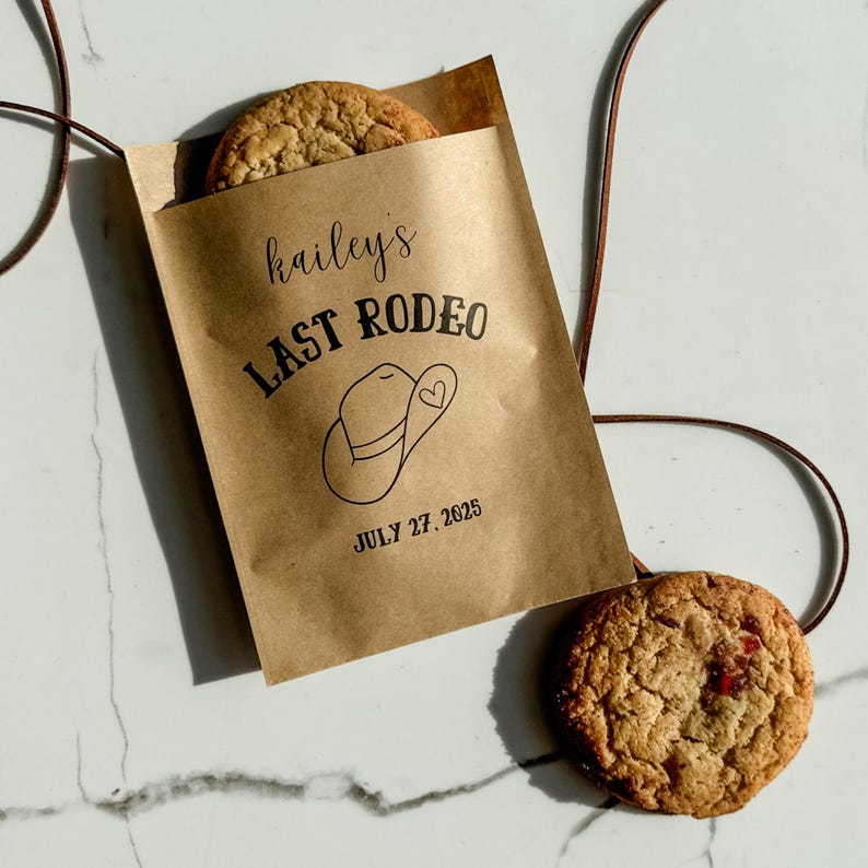 May include: A brown paper bag with the text "hailey's LAST RODEO" and a cowboy hat illustration. The date "JULY 27, 2025" is printed below. Two cookies are visible, one inside the bag and one outside.