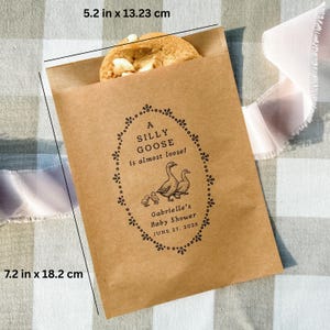 Puede incluir: Una bolsa de papel marr&oacute;n con una galleta. La bolsa tiene el texto "A SILLY GOOSE is almost loose!" y un dise&ntilde;o de baby shower. La bolsa mide 13,23 cm de ancho y 18,2 cm de alto.