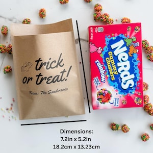 May include: A brown paper bag with the black text trick or treat! From: The Sandersons and a bat illustration, next to a box of Nerds Gummy Clusters candy. The bag measures 7.2 inches by 5.2 inches, surrounded by scattered colorful candy pieces.