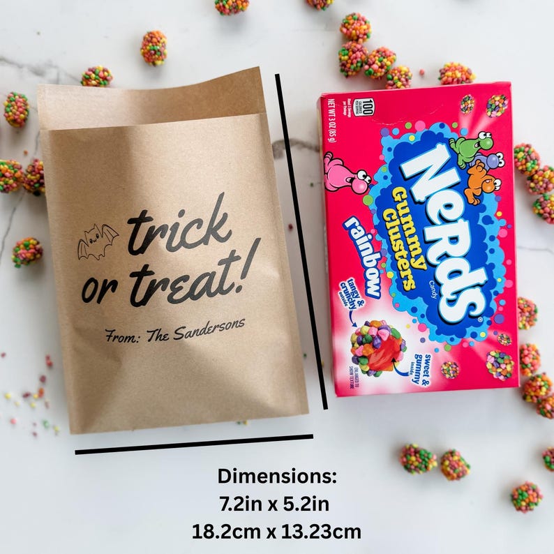 May include: A brown paper bag with the black text trick or treat! From: The Sandersons and a bat illustration, next to a box of Nerds Gummy Clusters candy. The bag measures 7.2 inches by 5.2 inches, surrounded by scattered colorful candy pieces.