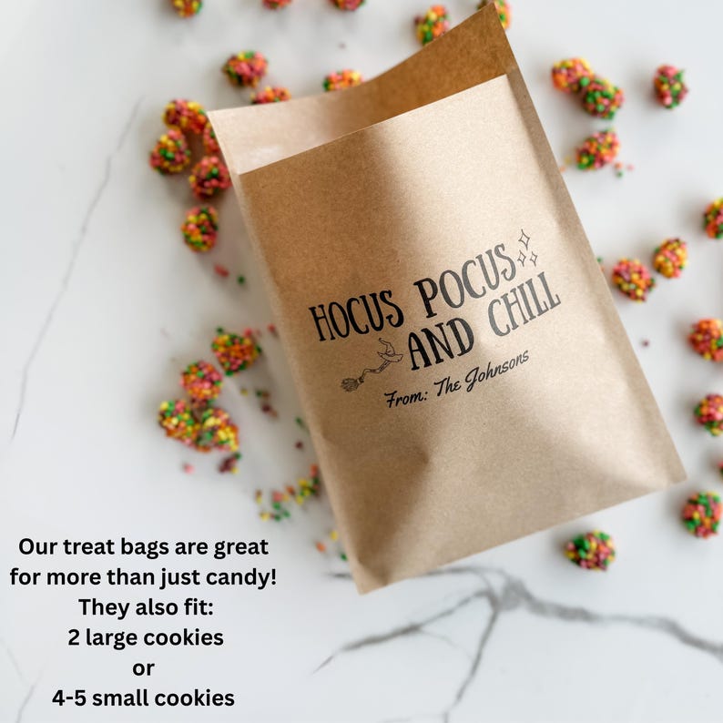 May include: A brown paper treat bag featuring the black printed text HOCUS POCUS AND CHILL with a small witch hat icon and the text From: The Johnsons. The bag is surrounded by scattered colorful candy pieces on a white marble surface.