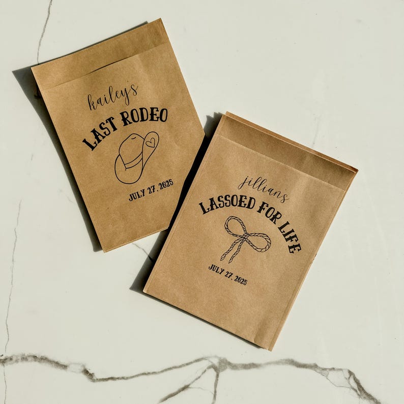 May include: Two brown paper favor bags with black text and illustrations. One bag reads "hailey's LAST RODEO" with a cowboy hat graphic and the date "JULY 27, 2025." The other bag says "jillians LASSOED FOR LIFE" with a lasso graphic and the same date.