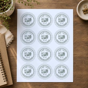 May include: A white sheet containing twelve circular stickers with a dark green graphic design. Each sticker features a mountain landscape, a tent, trees, and the text Camp Coco and Bachelorette Weekend with the date Sept 2024.