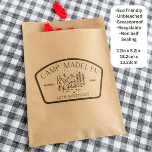 May include: A brown paper bag featuring a black printed graphic of mountains, trees, a tent, and the text Camp Madelyn March 12th Birthday 2026. The bag measures 7.2 inches by 5.2 inches and is described as eco-friendly, unbleached, and greaseproof.