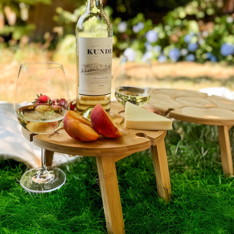 Outdoor wine table gift for wine lovers, showcasing foldable wooden design with cheese, grapes, and a full wine glass.