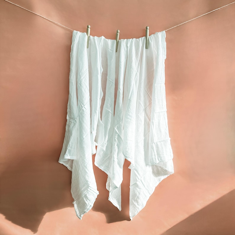 Puede incluir: Cuatro telas de algod&oacute;n blancas colgadas de un tendedero con pinzas de madera contra una pared de color melocot&oacute;n.