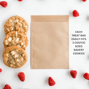 May include: Three large, golden-brown cookies with white chocolate chunks are arranged near a brown paper treat bag. Fresh red raspberries are scattered around the cookies and bag. Text on the bag reads: "EACH TREAT BAG EASILY FITS 3 COSTCO SIZED BAKERY COOKIES."