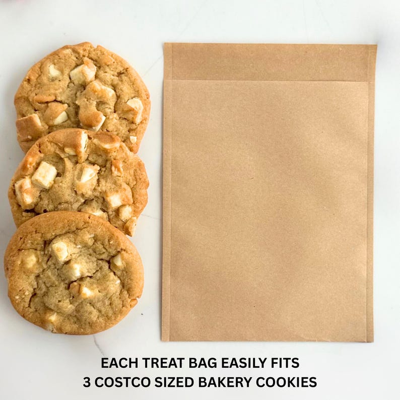 Puede incluir: Tres galletas grandes de color marr&oacute;n dorado con trozos de chocolate blanco junto a una bolsa de papel marr&oacute;n. El texto en la parte inferior dice: CADA BOLSA DE GOLOSINAS SE ADAPTA F&Aacute;CILMENTE A 3 GALLETAS DE PANADER&Iacute;A TAMA&Ntilde;O COSTCO.