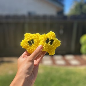 May include: Two yellow crocheted stars with black centers. The stars are held in a hand.