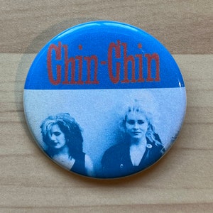 May include: A blue and white button with the text "Chin-Chin" in red lettering. The button features a black and white photo of two women.