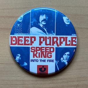 Op de afbeelding: Een ronde blauwe en witte knop met een afbeelding van de band Deep Purple. De naam van de band staat in rode letters en de albumtitel "Speed King" staat in rode letters. De albumtitel "Into the Fire" staat in zwarte letters. De namen van de bandleden staan onder hun foto's.