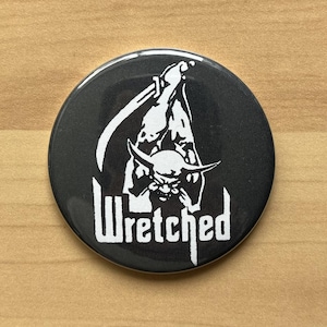 Puede incluir: Un botón negro y blanco con un gráfico de una criatura con cuernos y una guadaña. El texto "Wretched" está debajo del gráfico.