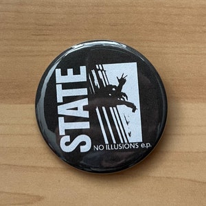 May include: Black and white button with the word "STATE" in large white letters and a graphic of a person with their arms raised. The text "NO ILLUSIONS e.p." is below the graphic.