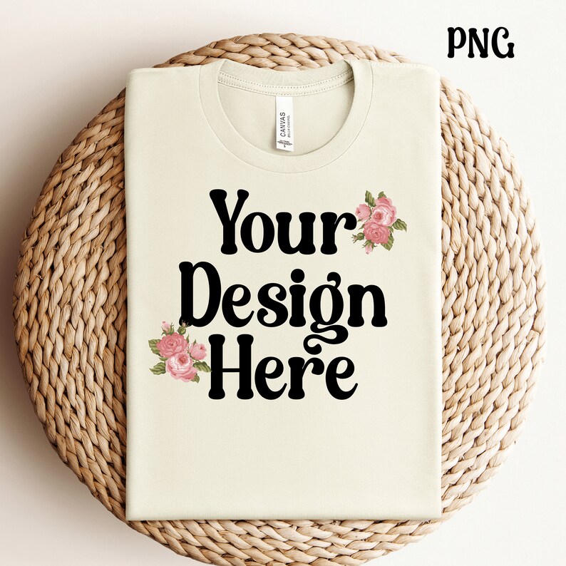 K&ouml;nnte beinhalten: Ein hellbeiges T-Shirt mit dem Text "Your Design Here" in Schwarz. Das Shirt hat ein florales Design mit rosa Blumen auf der Vorderseite.