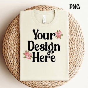 K&ouml;nnte beinhalten: Ein hellbeiges T-Shirt mit dem Text "Your Design Here" in Schwarz. Das Shirt hat ein florales Design mit rosa Blumen auf der Vorderseite.