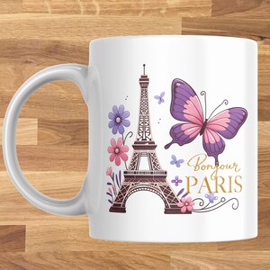 K&ouml;nnte beinhalten: Wei&szlig;e Keramiktasse mit einem Design mit dem Eiffelturm, Blumen und einem Schmetterling. Die Worte "Bonjour PARIS" sind in goldener Schrift geschrieben. Die Tasse hat einen gebogenen Griff.