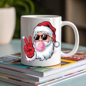 May include: White ceramic mug with a cartoon image of Santa Claus wearing sunglasses and blowing a bubble. Santa is giving the peace sign with his right hand.