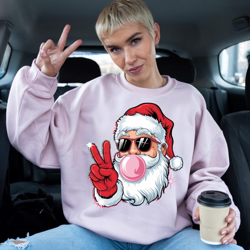 May include: Pink sweatshirt with a cartoon image of Santa Claus wearing sunglasses and blowing a bubble. Santa is giving the peace sign with his right hand.