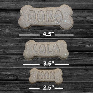 May include: Three dog bone-shaped biscuits with the names "Dora", "Lola", and "Max" written on them. The biscuits are 4.5 inches, 3.5 inches, and 2.5 inches long, respectively.