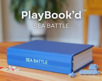 May include: A blue rectangular game box labeled PlayBook'd SEA BATTLE with white text on the cover and spine. Small gray plastic ship figurines and tiny red and white cylindrical game pieces are scattered on the surface next to the box.