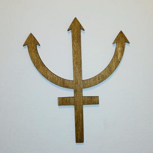 May include: A brown wooden wall decoration shaped like the astrological symbol for Neptune, featuring a central vertical shaft with a crossbar near the bottom and two curved arms extending upward, each ending in a pointed arrow tip.