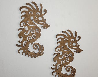 May include: Two dark brown wooden seahorse cutouts featuring intricate, swirling filigree patterns throughout their bodies. These flat, laser-cut decorative shapes display detailed fins, curled tails, and ornate designs on their surfaces.