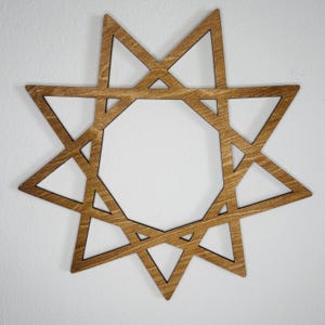 May include: A brown wooden wall decoration shaped like a nine-pointed star. The design features a central nonagon surrounded by nine interconnected triangular points, creating a geometric, open-frame structure with a visible wood grain texture.
