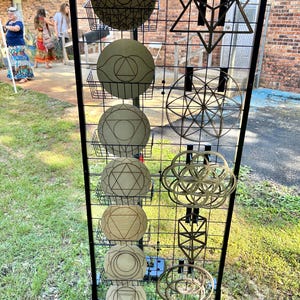 May include: A black metal grid display stand holding various wooden wall art pieces. The left side features seven circular plaques with engraved geometric patterns, while the right side displays four intricate, open-work geometric shapes.