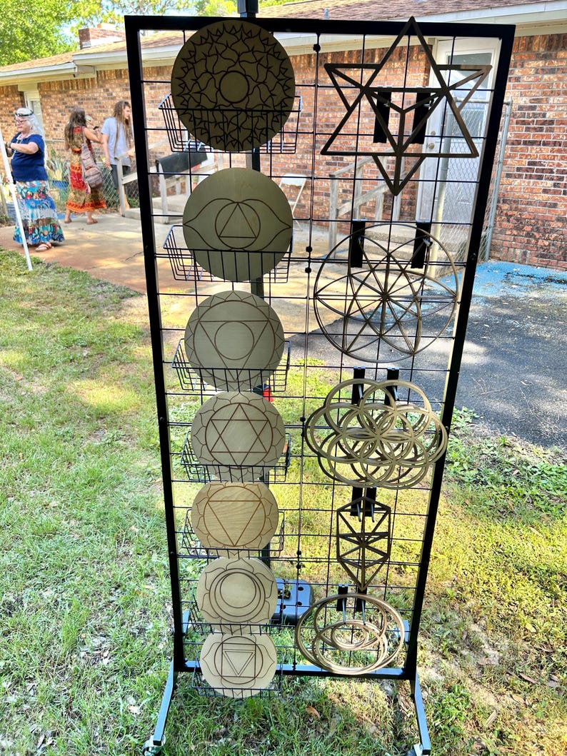 May include: A black metal grid display stand holding various wooden wall art pieces. The left side features seven circular plaques with engraved geometric patterns, while the right side displays four intricate, open-work geometric shapes.