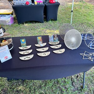 May include: A collection of laser-cut wooden items including crescent moon-shaped card holders, circular geometric mandalas, and a star-shaped ornament. The card holders feature moon phase engravings and hold various illustrated tarot-style cards.