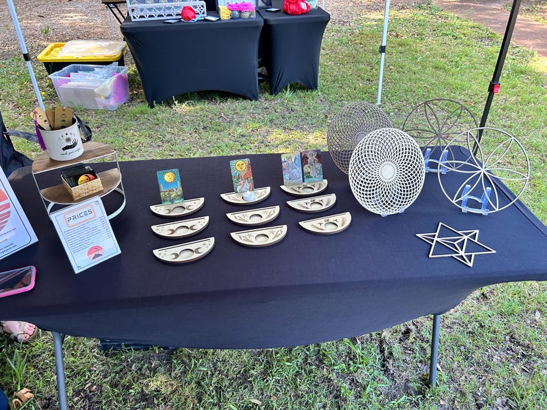 May include: A collection of laser-cut wooden items including crescent moon-shaped card holders, circular geometric mandalas, and a star-shaped ornament. The card holders feature moon phase engravings and hold various illustrated tarot-style cards.