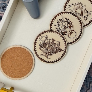 May include: Four circular coasters with a light wood finish and a serrated edge design. Three coasters feature dark brown laser-engraved anime-style character illustrations, while one coaster shows a plain brown cork surface on the reverse side.