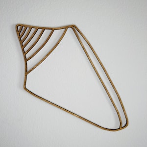 May include: A flat, brown, laser-cut wooden wall decoration shaped like a stylized seashell. The design features a hollow, open-frame construction with a series of parallel lines forming the spiral top section and a large, empty triangular body.