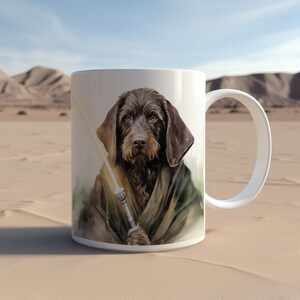 May include: White ceramic mug with a watercolor illustration of a brown dog wearing a green hooded robe and holding a lightsaber. The dog has a serious expression and is looking directly at the viewer.
