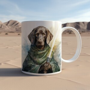 May include: A white ceramic mug featuring a brown dog wearing a green cloak and holding a lightsaber. The dog has a serious expression and is looking directly at the viewer. The background is a watercolour wash of blue and green.